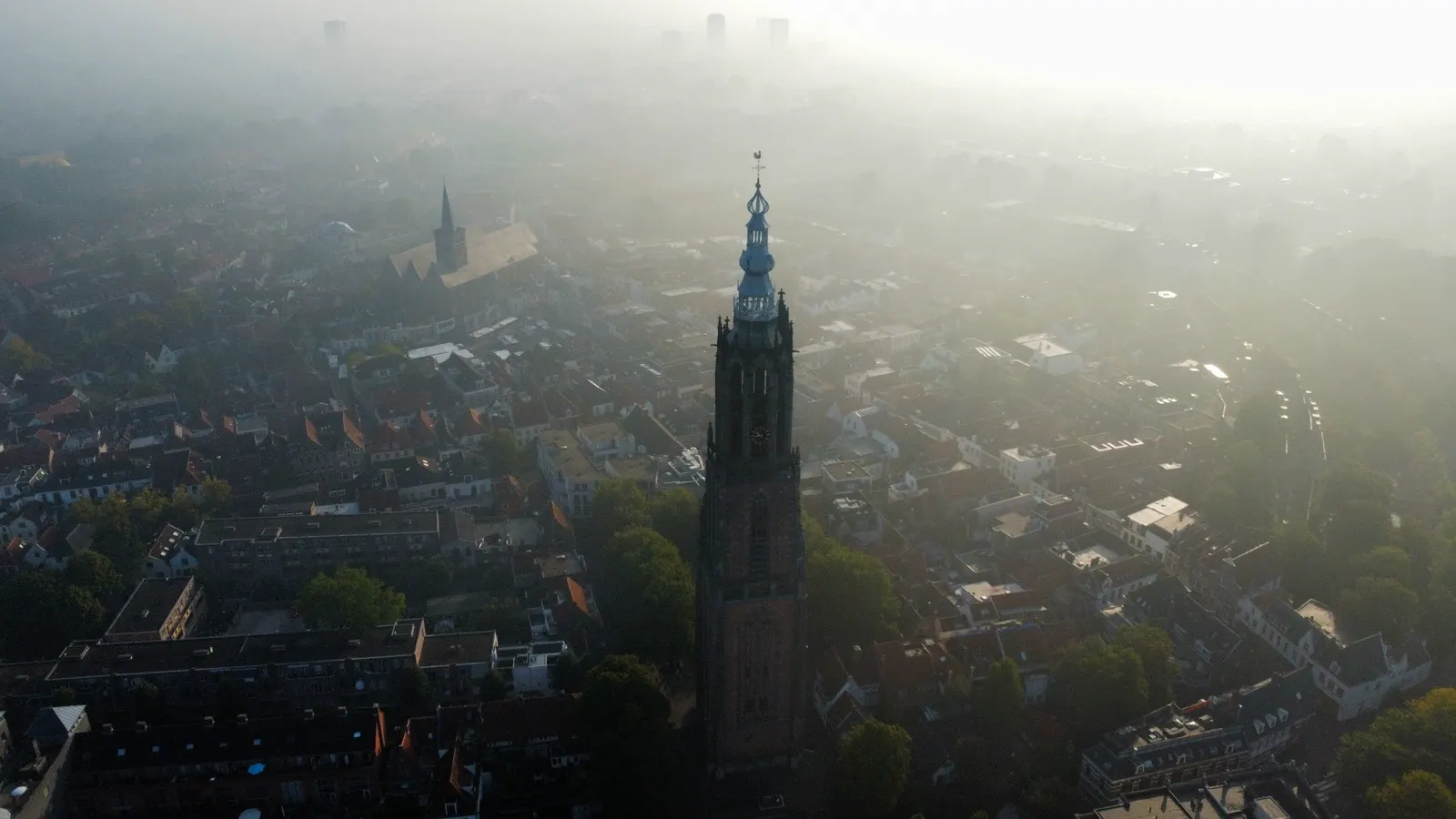 Dronebeeld van een kerktoren boven een stad in de mist